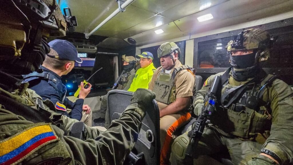 Geovany Andrés Rojas, alias Araña, in a tan uniform and vest, seated inside an armored vehicle between masked Colombian police officers