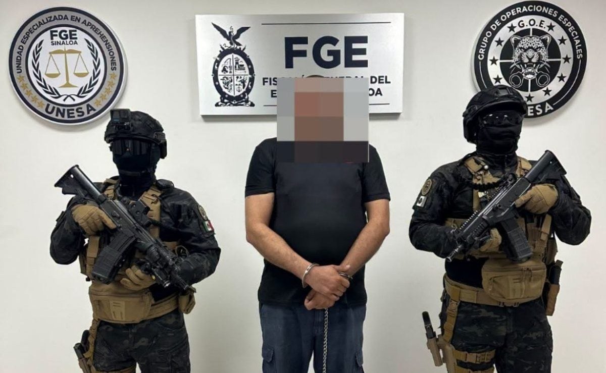 Florentino “N,” 44, stands handcuffed with his face pixelated between two armed agents in front of a Sinaloa state prosecutor's office (FGE) sign