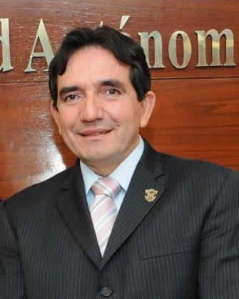 Portrait of Héctor Melesio Cuén Ojeda in a dark suit and striped tie in front of a Universidad Autónoma de Sinaloa sign