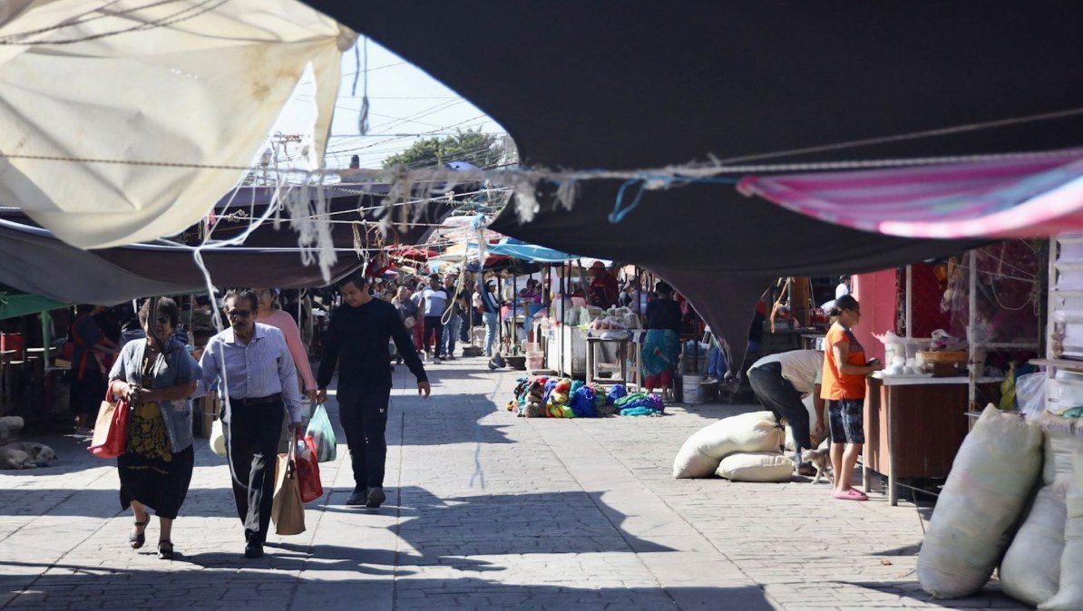 Shoppers walk through a shaded street market lined with stalls and sacks of goods in Juchitán, Oaxaca.