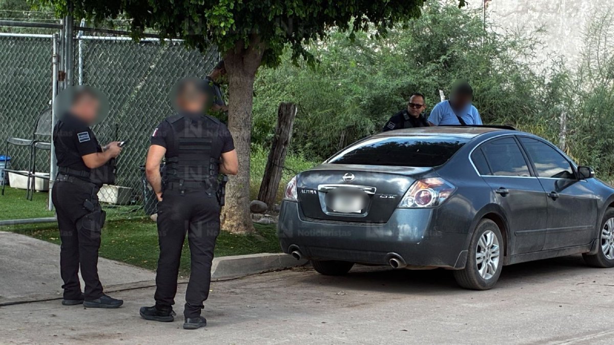Police officers stand beside a gray Nissan Altima at a fenced home in the Ampliación 12 de Octubre neighborhood of Los Mochis, Sinaloa, after the Sept. 28, 2026 shooting