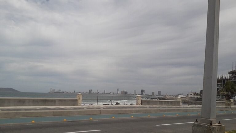 Seafront boulevard in Mazatlán, Sinaloa, under an overcast sky, with the city skyline across the water