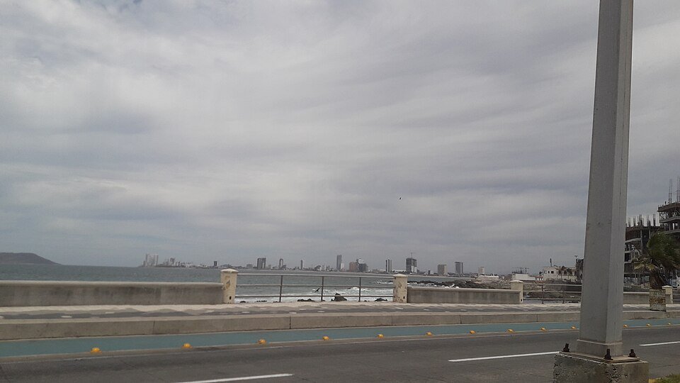 Seafront boulevard in Mazatlán, Sinaloa, under an overcast sky, with the city skyline across the water