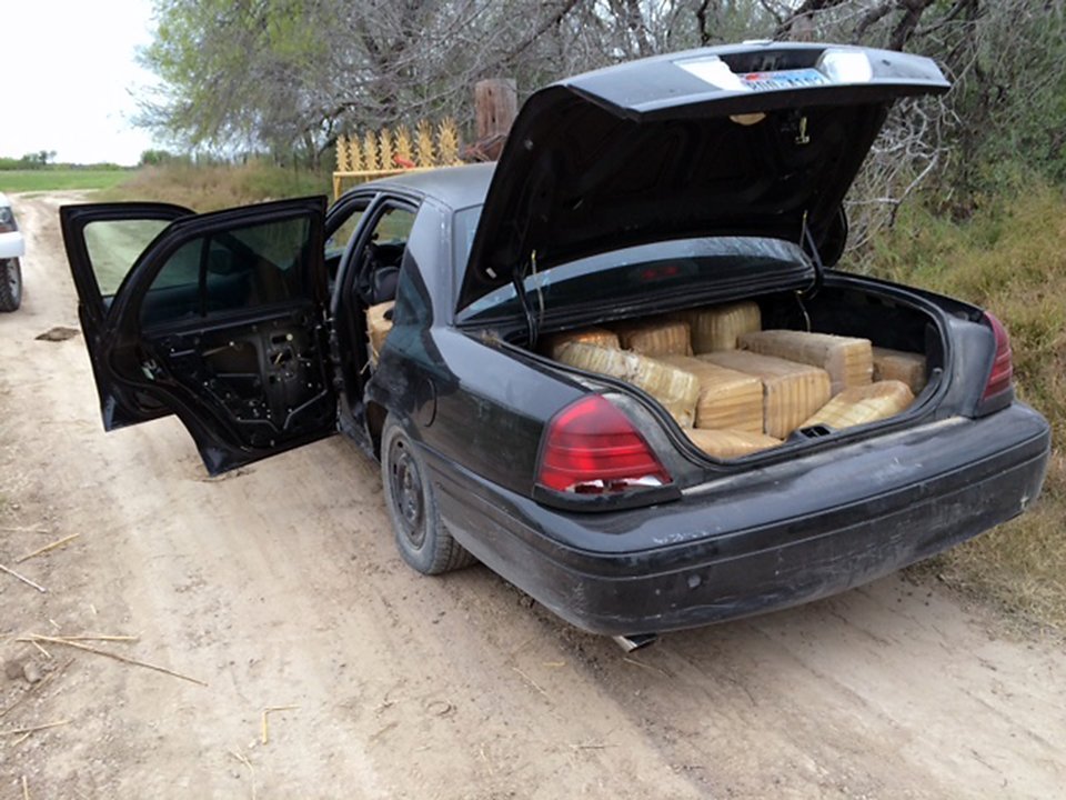 Bundles of marijuana packed in the open trunk of a seized black sedan on a dirt road in the Rio Grande Valley