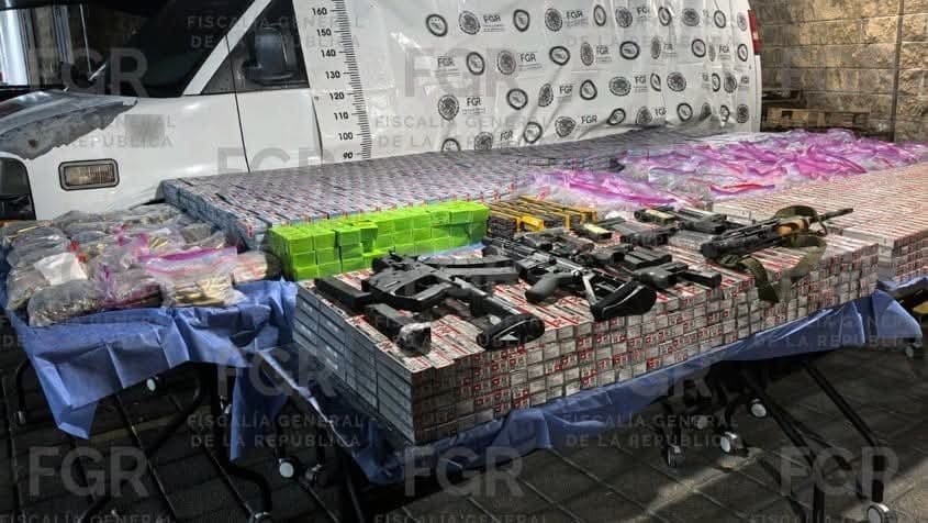 Rifles, pistols and stacked ammunition boxes displayed in front of a white pickup by Mexico's FGR