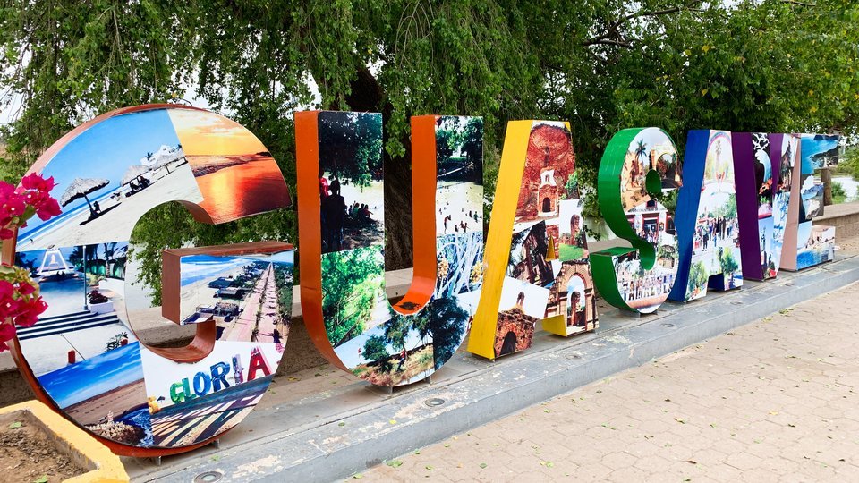 Large colorful letters spelling Guasave, decorated with photos of local landmarks, under trees in Guasave, Sinaloa