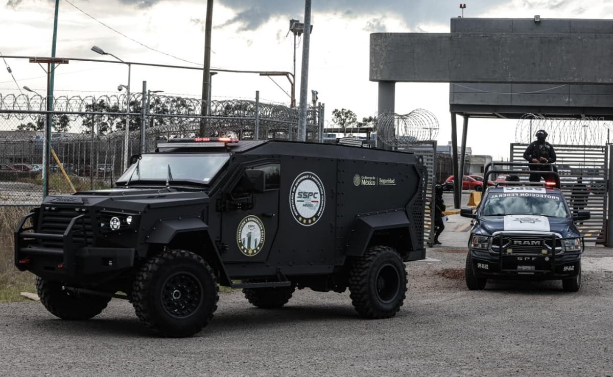 Black armored federal security vehicle and a federal protection pickup at the gate of El Altiplano prison
