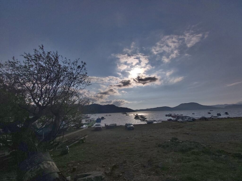 Lake at Avándaro, Valle de Bravo, State of Mexico, with boats and parked cars on the shore under a cloudy sky