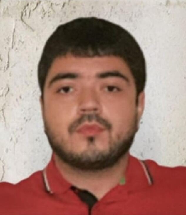 Head-and-shoulders photo of a young bearded man in a red polo shirt against a white wall