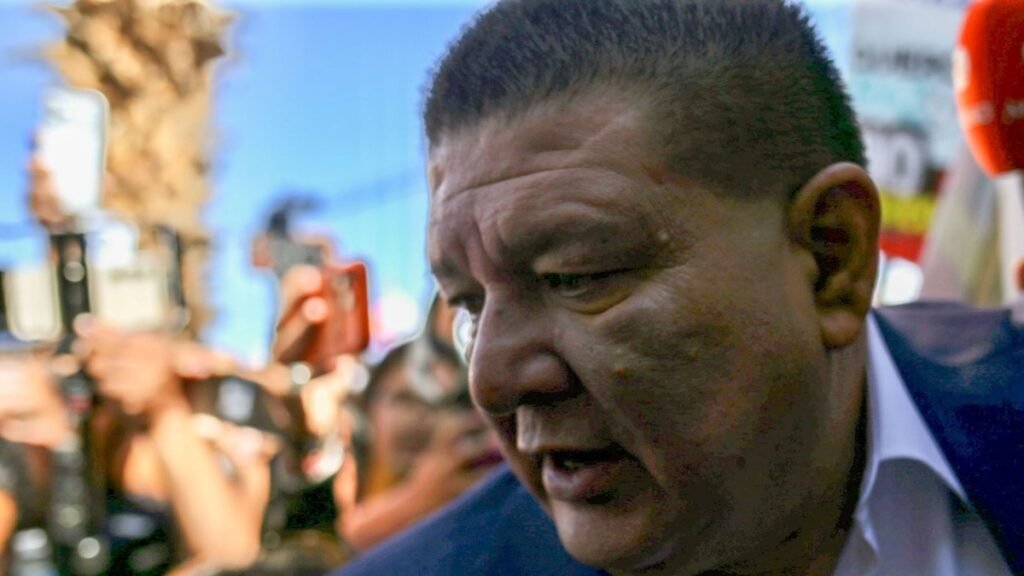 Former Chihuahua state prosecutor César Jáuregui Moreno surrounded by reporters holding phones and microphones