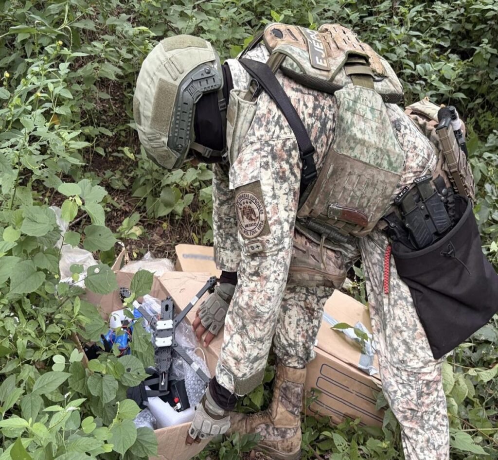 Mexican Army special forces soldier bends over a cardboard box holding a carbon-frame drone in brush in Concordia, Sinaloa