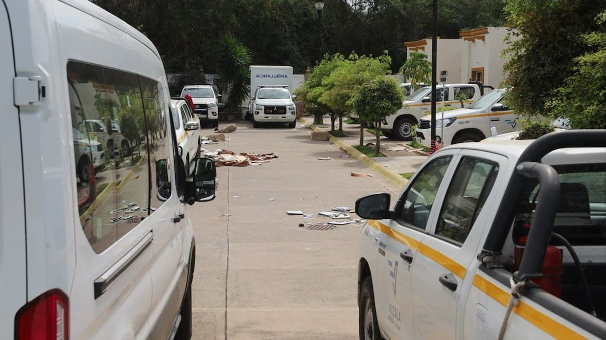 Vizsla Silver pickup trucks and a van parked along a street inside the company's gated residential compound in Concordia, Sinaloa, with debris scattered on the pavement