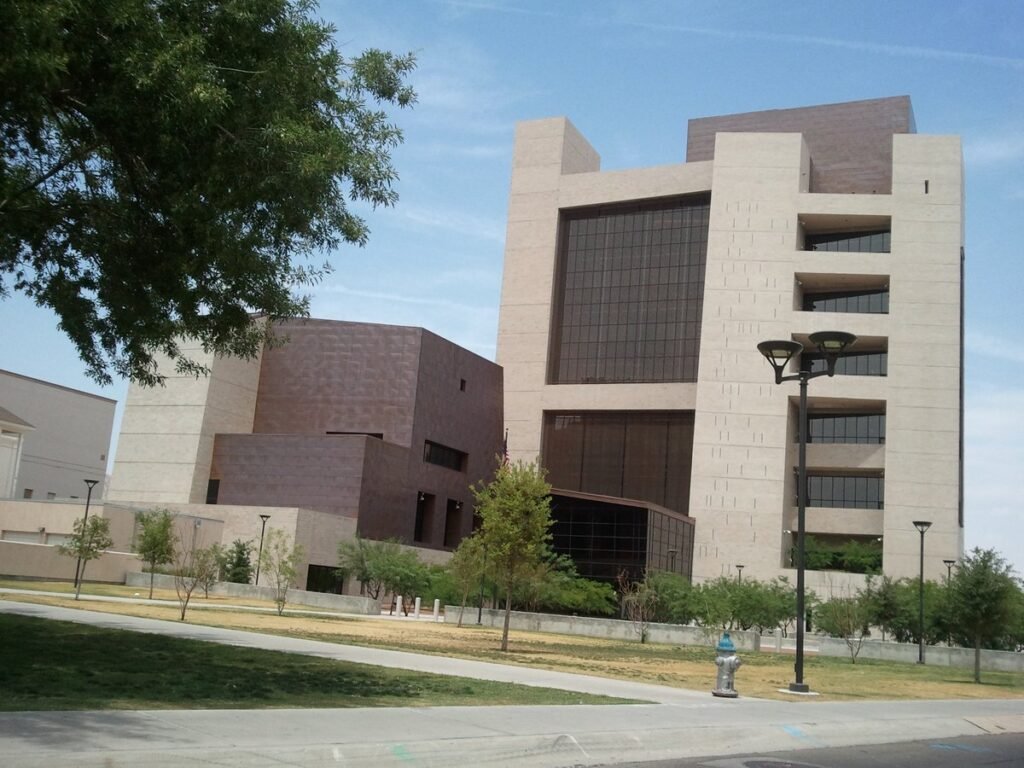 The Albert Armendariz Sr. United States Courthouse in El Paso, Texas, a tall tan stone and dark glass building behind trees and a lawn