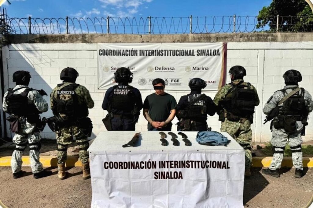 Jesús Abraham 'N,' 'El Talibán,' handcuffed with his eyes blacked out between soldiers and Sinaloa state police, with a rifle and magazines on a table