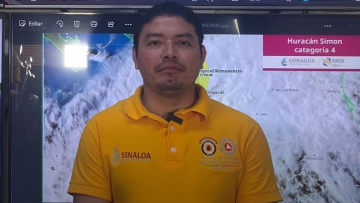 Escuinapa Civil Protection coordinator Jesús López Bibriesca in a yellow Sinaloa Civil Protection shirt in front of a Hurricane Simon forecast screen