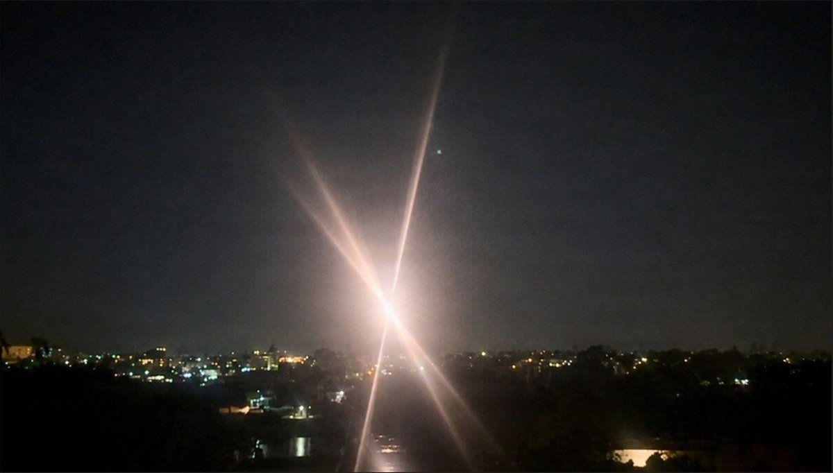 A bright starburst of light in a night sky above city lights, showing an Army high-energy laser engaging a drone