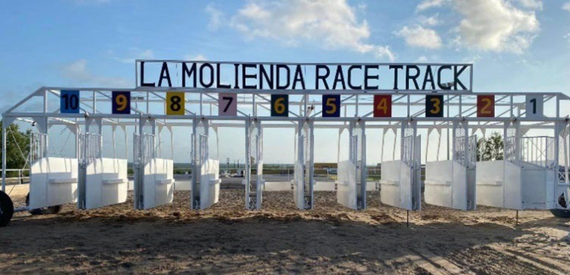 White ten-stall starting gate under a 'La Molienda Race Track' sign on a dirt horse track outside Nuevo Laredo