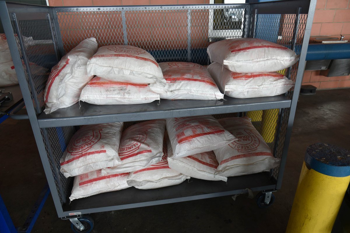 Two-shelf metal cart holding about 20 white sacks with red printing, stacked at a CBP inspection area