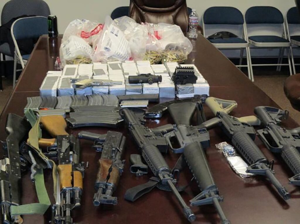 AK- and AR-style rifles, magazines, boxed ammunition and bags of loose rounds laid out on a conference table