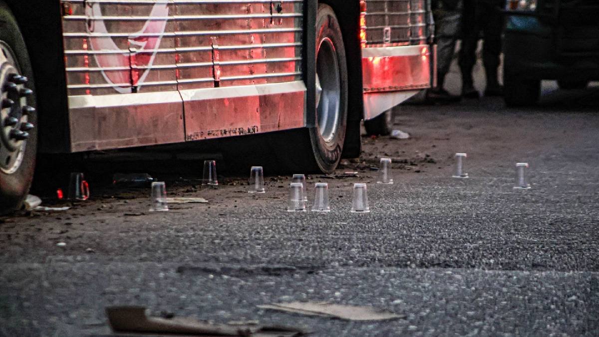 Clear plastic cups placed on asphalt as evidence markers beside a parked bus at a crime scene