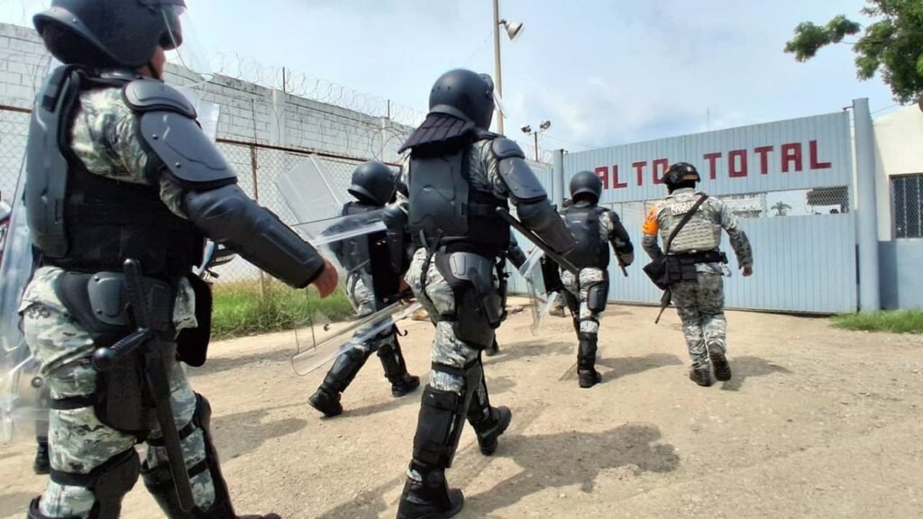 National Guard officers in riot gear with shields walk toward the gate of El Castillo prison in Mazatlán, Sinaloa