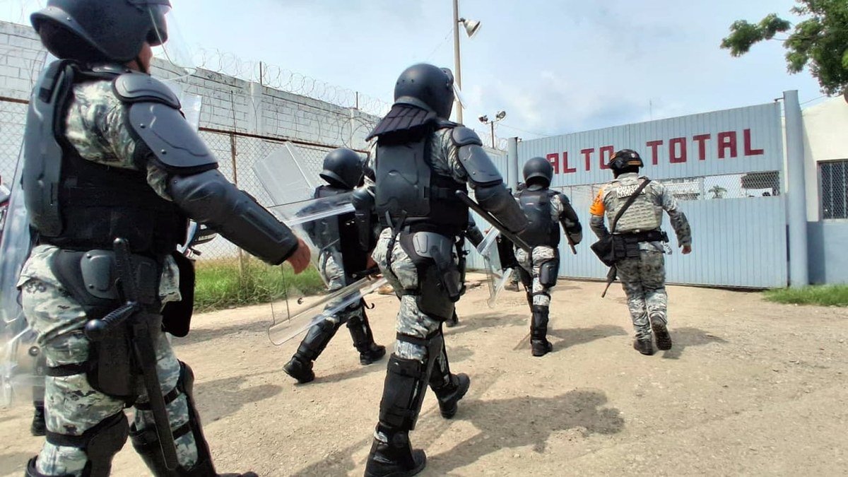 National Guard officers in riot gear with shields walk toward the gate of El Castillo prison in Mazatlán, Sinaloa