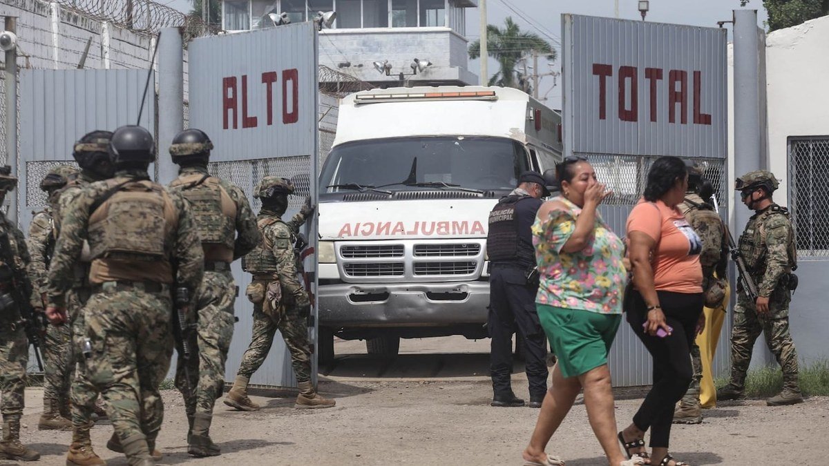 Soldiers, a municipal police officer and an ambulance at the gate of El Castillo prison in Mazatlán, Sinaloa, as two women walk past