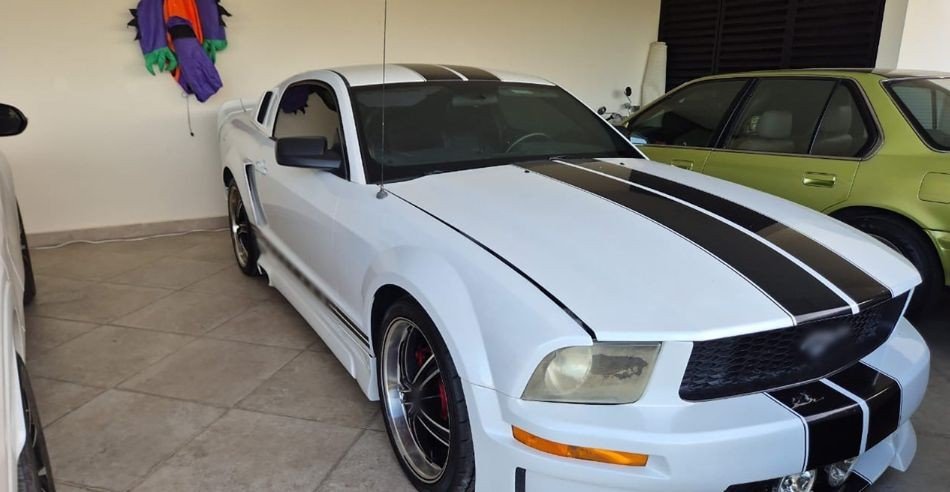 A white sports car with black racing stripes parked in a covered garage next to a green sedan