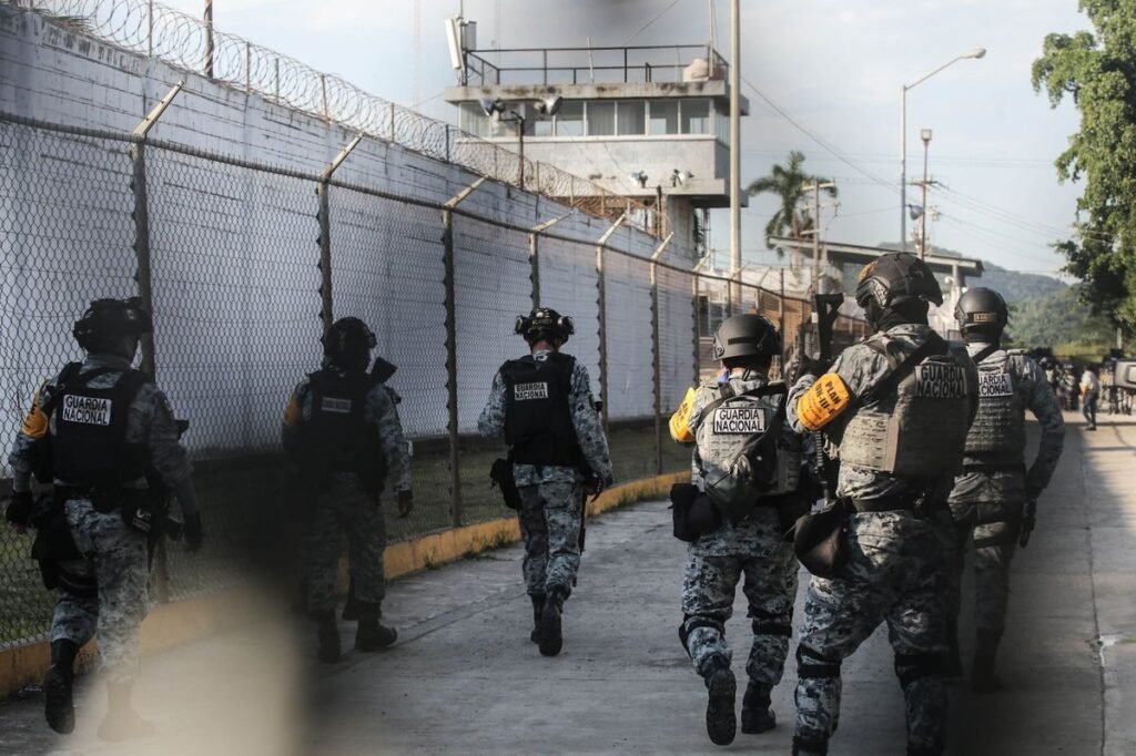 National Guard officers in tactical gear walk along the fenced perimeter of a prison with a guard tower in Mazatlán, Sinaloa