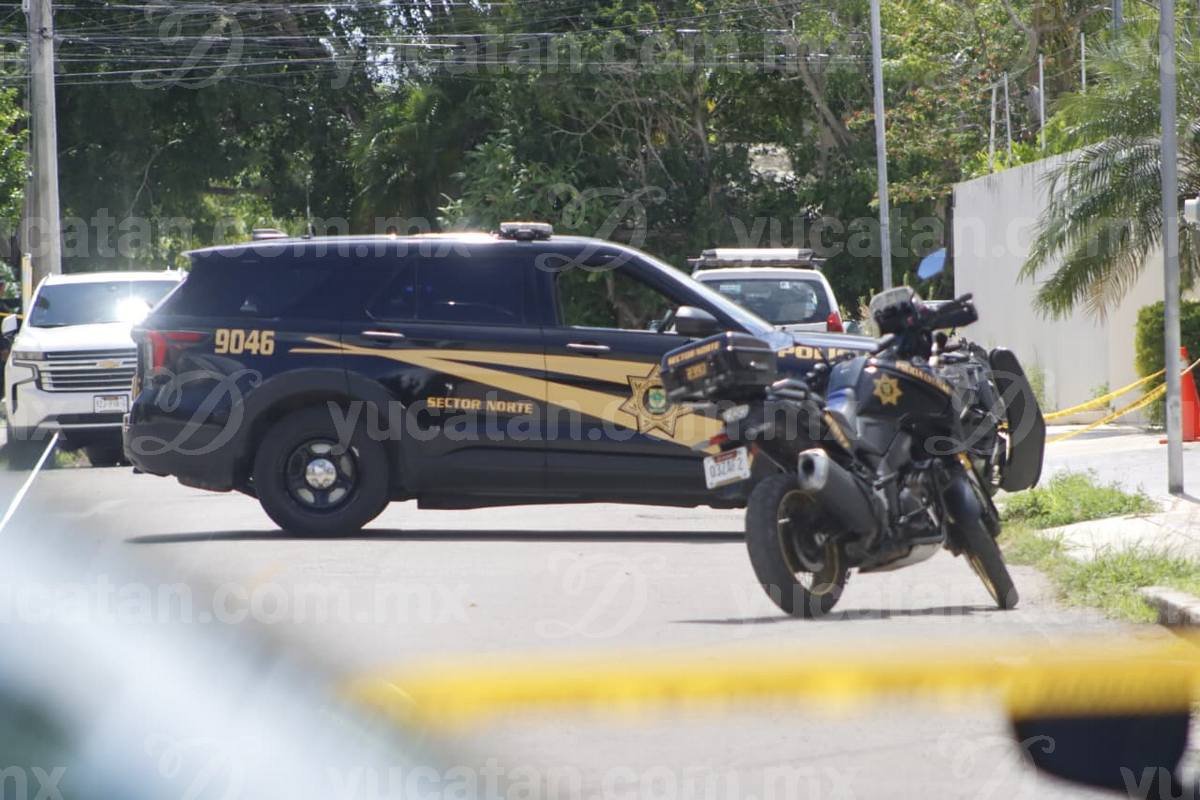 A black-and-gold Yucatán state police SUV and police motorcycle parked behind yellow crime-scene tape on a residential street in north Mérida.