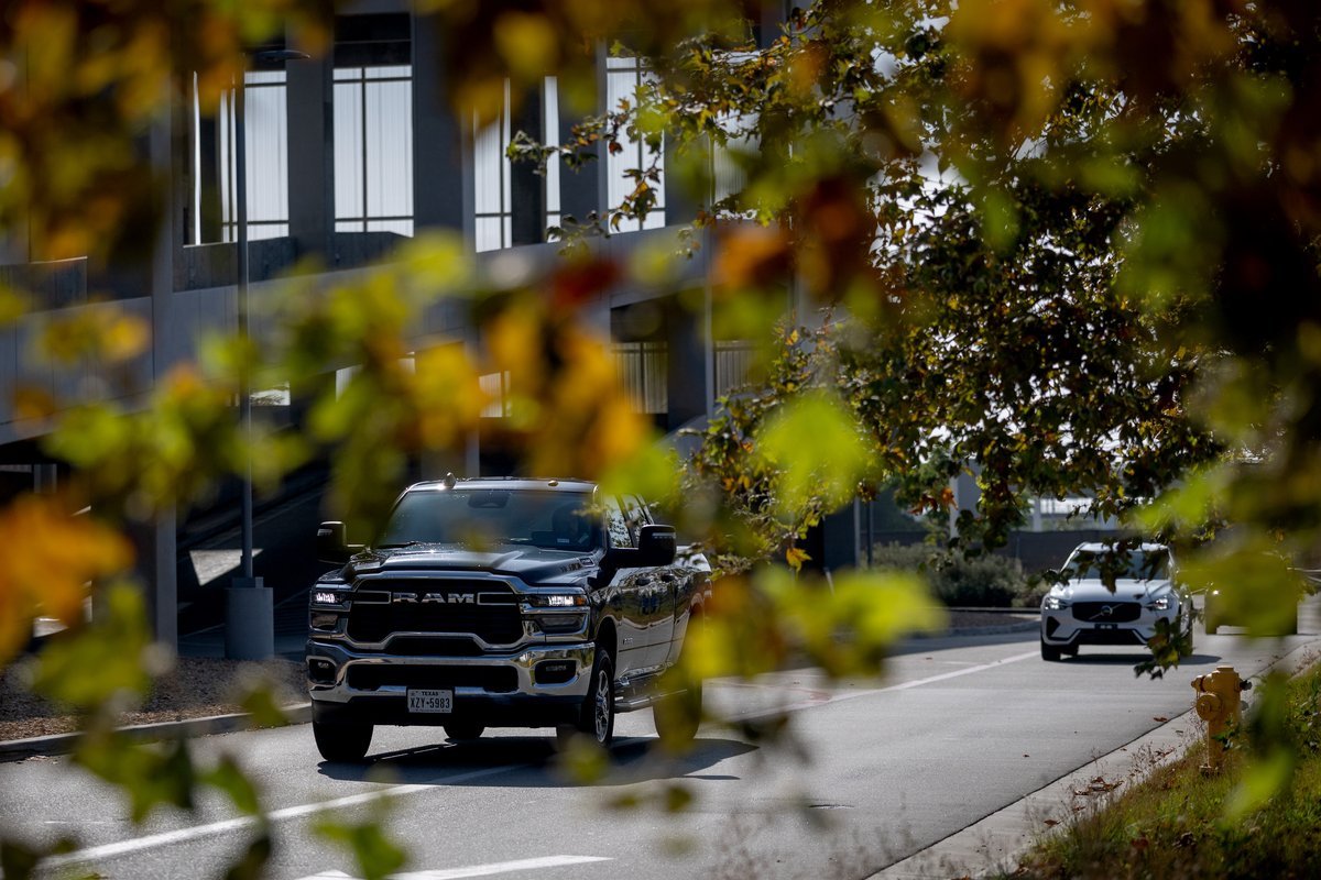 A black Ram heavy-duty pickup truck with Texas plates drives out of the LAX Rental Car Center in Los Angeles, framed by autumn leaves