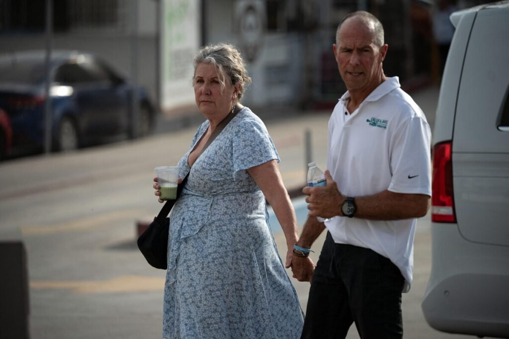 Debra Robinson, in a blue floral dress, and Martin Robinson, in a white polo shirt, walk side by side on a street in Ensenada