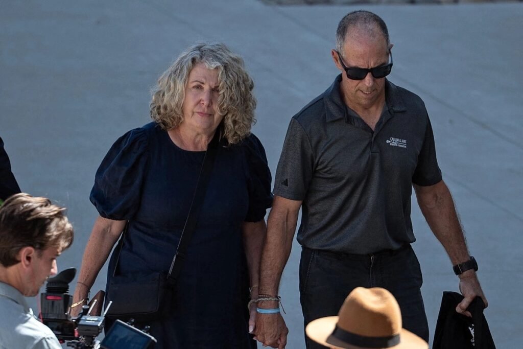 Debra Robinson, in a dark blue dress, and Martin Robinson, in a gray Callum & Jake Robinson Foundation polo and sunglasses, walk hand in hand in Ensenada