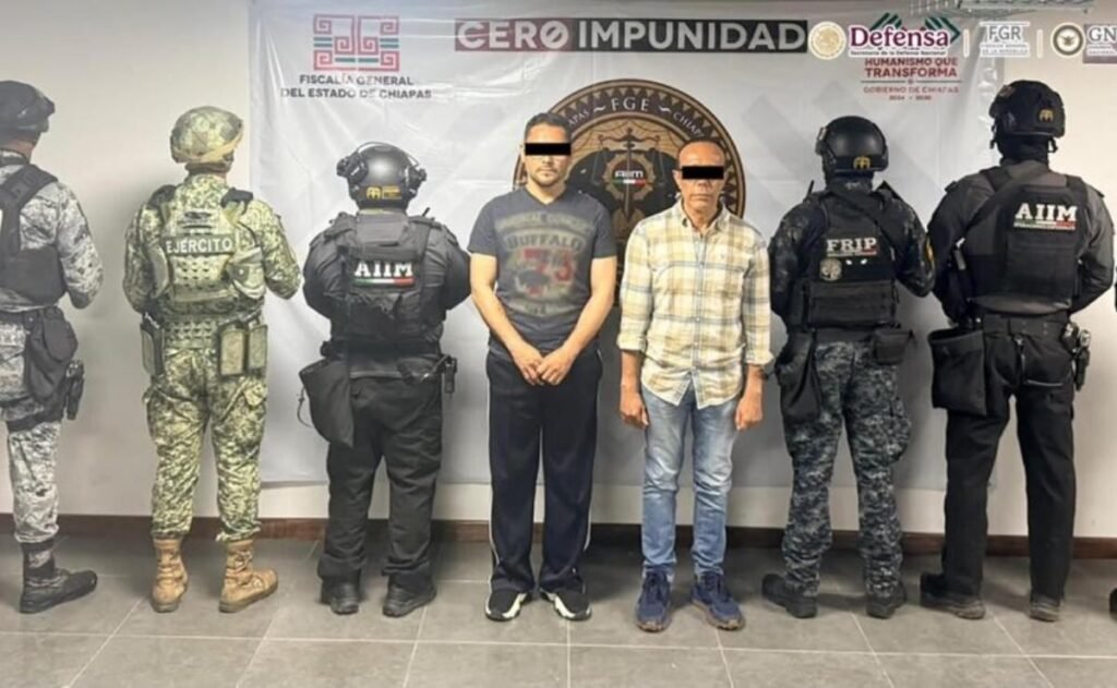 Two arrested men, their eyes covered with black bars, stand between Mexican soldiers and Chiapas state agents in front of a Chiapas Attorney General's Office banner