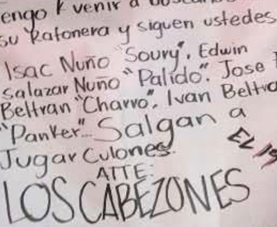 Handwritten white sign with a Spanish threat naming Isac Nuño 'Soury', Edwin Salazar Nuño 'Pálido', José F. Beltrán 'Charro' and Iván Beltrán 'Panker', signed 'Los Cabezones' and 'El 19'