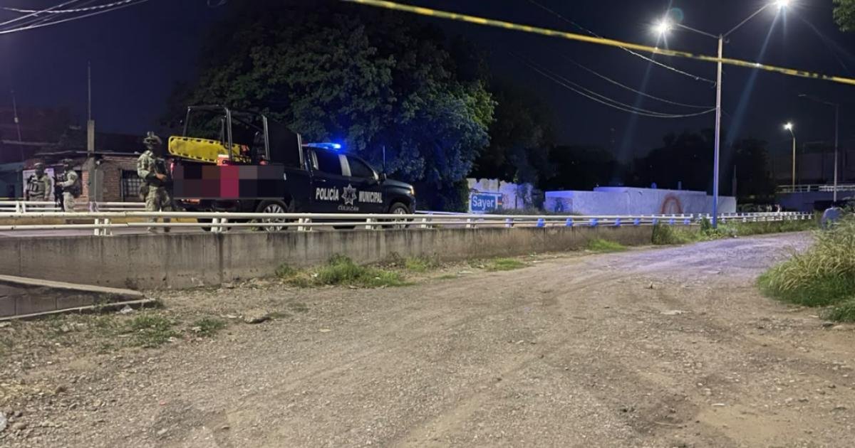 Culiacán municipal police pickup and soldiers behind crime-scene tape on a road at night, seen from a dirt lot