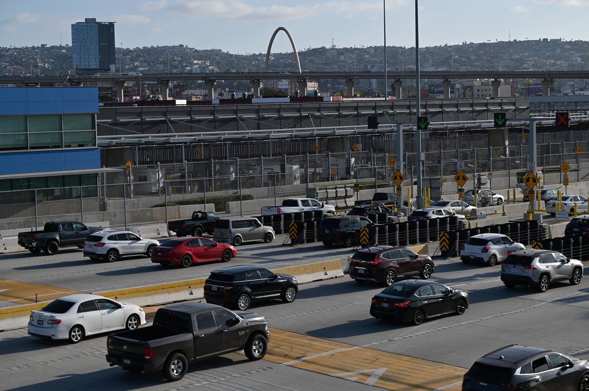 Lines of cars, SUVs and pickups at the San Ysidro Port of Entry crossing into Tijuana, with the city's hillsides and arch landmark behind
